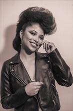 A vertical grayscale of a cute young smiling hipster female in a leather jacket posing at the camera