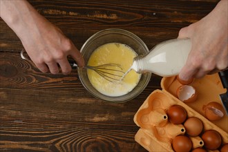 Top view of pouring milk in eggs. Preparation of an omelette