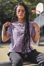 Seductive look of young dark-skinned woman in purple shirt holding long braids