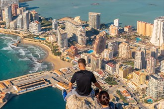 A young man sitting on top of the Penon de Ifach Natural Park with the city of Calpe in the background