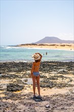 A young tourist wearing a hat on the beaches of the Corralejo Natural Park with the sea in the background