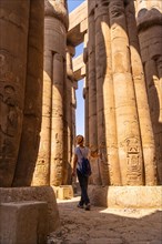 A young tourist in a white t-shirt and hat looking at ancient egyptian drawings on the columns of the Temple of Luxor
