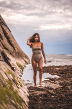 A dark-haired caucasian woman in a brown swimsuit on a natural background by the sea in the town of Zumaia