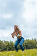 Fitness session with a young blonde caucasian woman exercising in nature with a blue maya on her feet and a white short shirt. Squatting and jumping