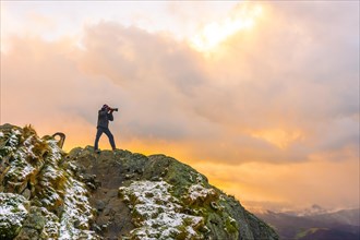 A photographer on top of the mountain in the snowy winter orange sunset