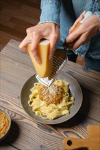 High angle view of female hands grating parmesan cheese into pasta
