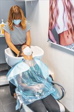 Hairdresser with face mask washing hair to client. Safety measures for hairdressers in the Covid-19 pandemic. New normal