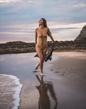 A brunette woman having fun with a swimsuit and a pareo walking along the beach in summer in the cloudy sunset