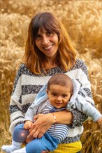 A young smiling mother with her baby in a yellow straw field in French Brittany in the summer of July