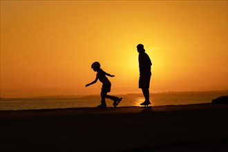 Silhouette of a man and a child skating on skateboard and roller skates. Mid shot