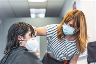 Hairdresser with face mask cutting bangs to the client. Safety measures for hairdressers in the Covid-19 pandemic. New normal