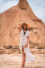 A brunette Caucasian girl with an explorer outfit with a white dress walking enjoying the desert of Las Bardenas Reales in Navarra. Spain