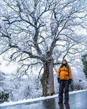 A young woman in a yellow jacket in a snowy tree on an icy road. Snow in the town of Opakua near Vitoria in Araba