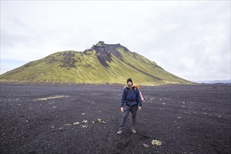 A young man in volcanic ash and a green mountain in the background on the 54 km trek from Landmannalaugar