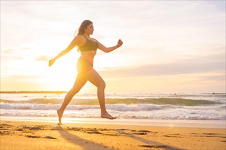 Horizontal photo with copy space of the side view of a woman jogging along a beach during sunset