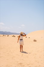 A young tourist wearing a hat walking along the sand on the beaches of the Corralejo Natural Park