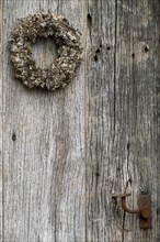 Very old weathered wooden door with a wreath of twigs and lichen