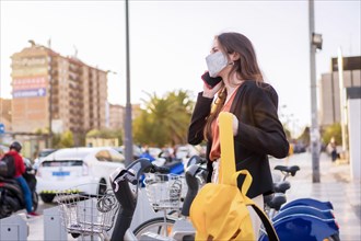 Woman using facial mask while talking to the mobile and using public bike