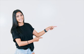 Cheerful teen girl pointing an offer isolated. Beautiful young girl pointing to a banner to the side. Happy latin woman pointing a promo isolated