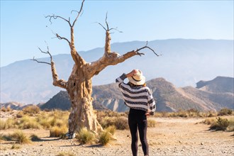 A young hiker girl with a hat visiting the tree of misfortune in the desert of Tabernas