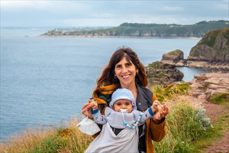 A young mother with her baby at the Phare Du Cap Frehel is a maritime lighthouse in Cotes-dÂ´Armor France . At the tip of Cap Frehel