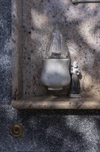 Monk figure next to an electric candle on a grave in a cemetery
