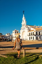 A young woman with a hat sitting and looking at the El Rocio sanctuary at the Rocio festival