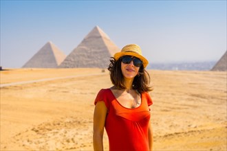 Portrait of a young tourist in red dress enjoying the pyramids of Giza