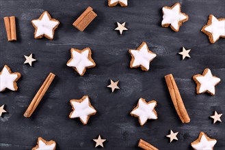 Traditional German star shaped glazed cinnamon Christmas cookies called 'Zimtsterne' on dark black background with star ornaments and cinnamon sticks