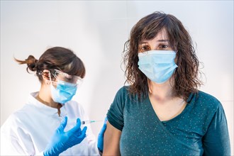 A woman doctor with a face mask applying the coronavirus vaccine to a young woman at risk. First vaccines for people at risk