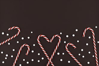 Christmas candy canes forming heart surrounded by white snowball ornaments on dark background