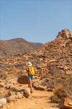 A hiker with a hat and yellow backpack walking along the canyon path towards the Mirador de la Penitas