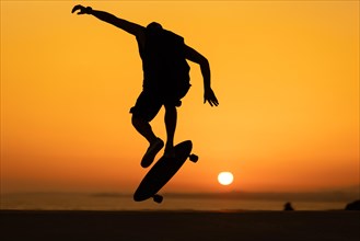 Silhouette of a man performing a skateboarding trick at bright orange sunset. Mid shot