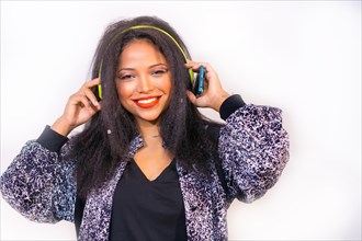 A portrait of a smiling Hispanic attractive woman on headphones holding a phone and choosing a song to play