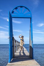 A cheerful young girl at a blue door in the Caribbean Sea on Roatan Island. Honduras