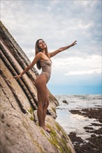 A dark-haired caucasian woman in a brown swimsuit on a natural background by the sea in the town of Zumaia