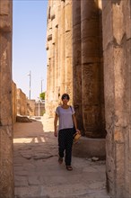 A young tourist in a white t-shirt and hat visiting the temple and looking at the ancient egyptian drawings on the columns of the Luxor Temple