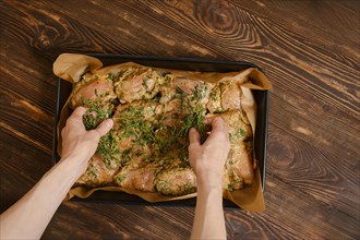 Hands of woman scattering thyme over marinated chicken thighs in baking tray