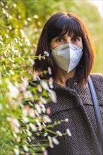 Portrait of a young woman with a mask next to a beautiful daisies. First walks of the uncontrolled Covid-19 pandemic