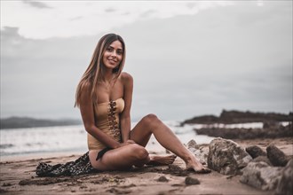Fashion posing of a brunette woman in a swimsuit and a pareo on the beach in summer