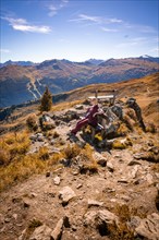 Wanders' woman on bench at summit cross in rocky mountain landscape in autumn
