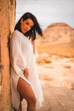 Brunette Caucasian girl in a white dress in a perched in a house in the desert