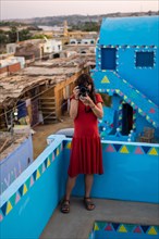 A young woman looking at the village from a beautiful terrace of a traditional blue house in a Nubian village along the Nile river and near Aswan city. Egypt