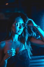 Portrait of a brunette girl at night in the city with blue leds and blue glasses