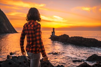 A young woman in a plaid shirt watching the sunset from the Pasajes San Juan lighthouse