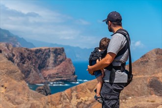 A father with his baby in his backpack in Ponta de Sao Lourenco looking at the landscape and the sea