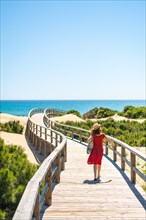 Girl with red dress on the wooden path to Playa Moncayo in Guardamar del Segura next to Torrevieja
