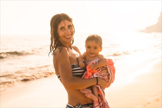 A smiling mother with her six-month-old baby at sunset on a beach