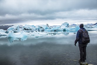 A young man with a backpack looking at the Jokulsarlon Ice Lake in the golden circle of southern Iceland