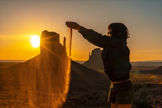 A brunette lifestyle girl at the dawn of Monument Valley throwing sand between her hands